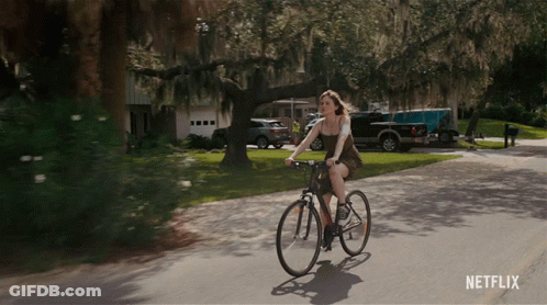 A Woman Is Riding A Bike Down A Street With A Netflix Logo On The Bottom GIF