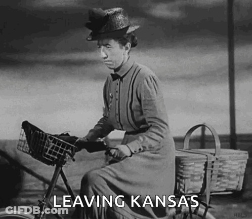A Woman Is Riding A Bike With The Words Leaving Kansas Written On It GIF