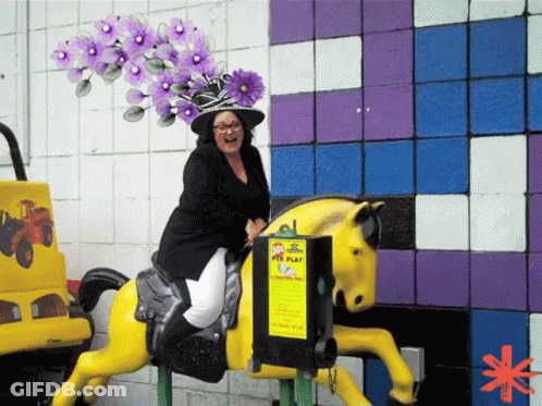 A Woman Is Riding A Yellow Horse In Front Of A Sign That Says ' Kids Play ' On It GIF