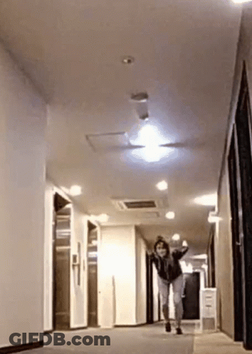 A Woman Is Running Down A Hallway In A Building . GIF
