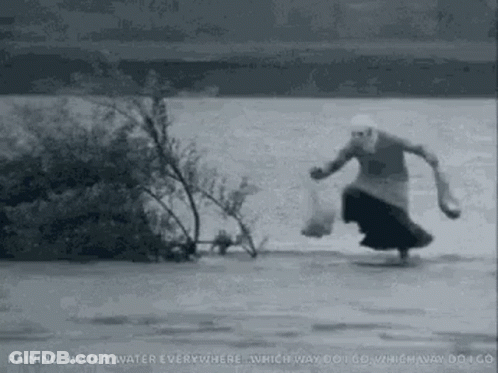 A Woman Is Running Through A River Carrying A Bag Of Food . GIF