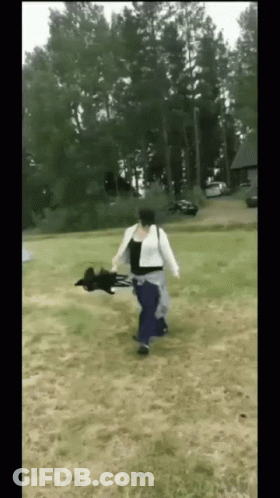 A Woman Is Running With A Black Dog In Her Arms In A Field GIF