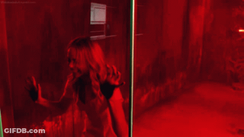 A Woman Is Screaming Behind A Glass Door With A Red Light Behind Her GIF