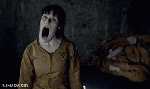 A Woman Is Screaming In A Dark Room With A Triangle Logo On Her Jacket GIF