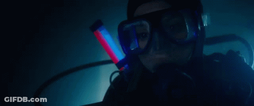 A Woman Is Scuba Diving In A Dark Room With A Red Light In Her Mouth . GIF