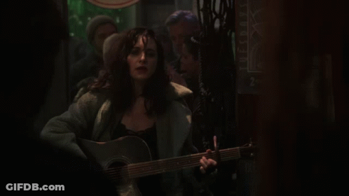 A Woman Is Singing And Playing A Guitar In Front Of A Sign That Says Tuesdays GIF