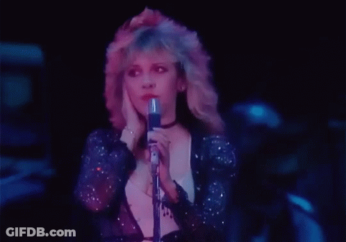 A Woman Is Singing Into A Microphone In A Dark Room . GIF