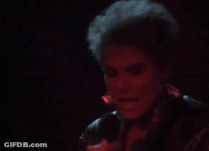 A Woman Is Singing Into A Microphone In A Dark Room With Red Lights Behind Her . GIF