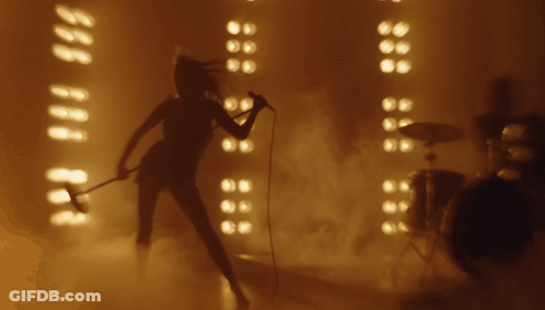 A Woman Is Singing Into A Microphone In Front Of A Drum Set GIF