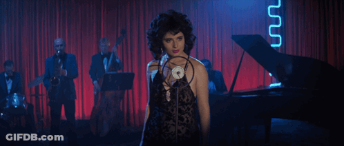 A Woman Is Singing Into A Microphone In Front Of A Piano GIF