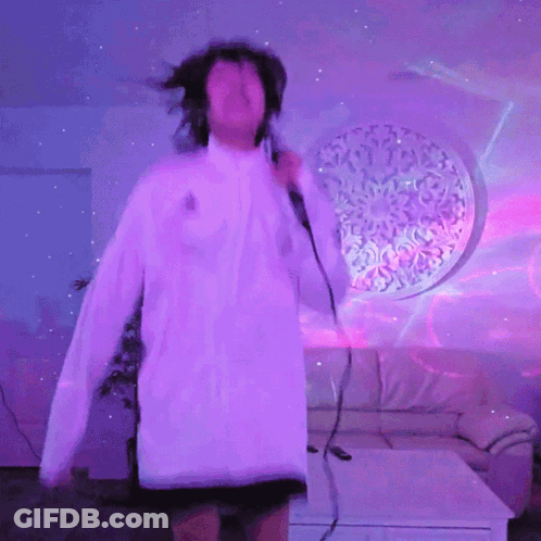A Woman Is Singing Into A Microphone In Front Of A Purple Wall GIF