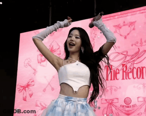 A Woman Is Singing Into A Microphone In Front Of A Sign That Says The Record GIF
