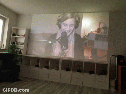 A Woman Is Singing Into A Microphone On A Large Screen GIF