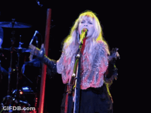 A Woman Is Singing Into A Microphone On A Stage GIF