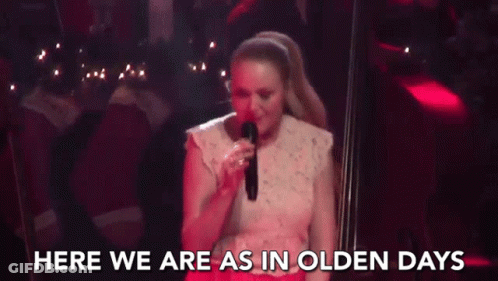 A Woman Is Singing Into A Microphone On A Stage And The Words `` Here We Are As In Olden Days '' Are Behind Her . GIF