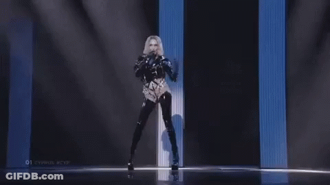 A Woman Is Singing Into A Microphone On A Stage In Front Of A Blue And White Wall . GIF