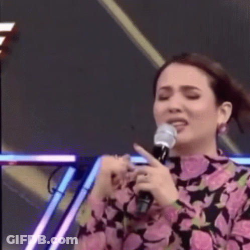 A Woman Is Singing Into A Microphone On A Stage While Making A Funny Face . GIF
