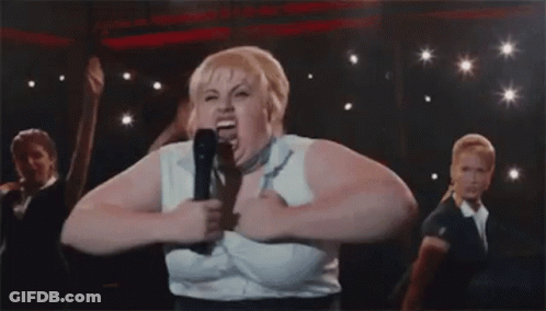 A Woman Is Singing Into A Microphone On A Stage With Other People . GIF