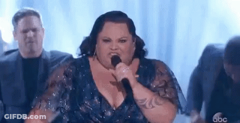 A Woman Is Singing Into A Microphone On Stage . GIF