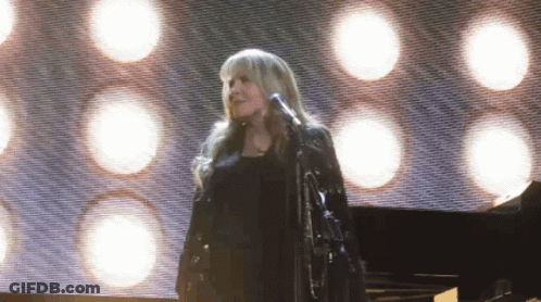 A Woman Is Singing Into A Microphone On Stage GIF