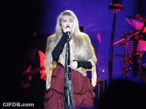 A Woman Is Singing Into A Microphone On Stage GIF