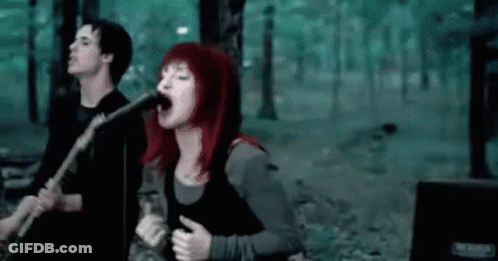 A Woman Is Singing Into A Microphone While A Man Plays A Guitar . GIF