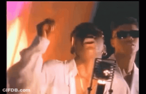 A Woman Is Singing Into A Microphone While A Man Stands Behind Her . GIF