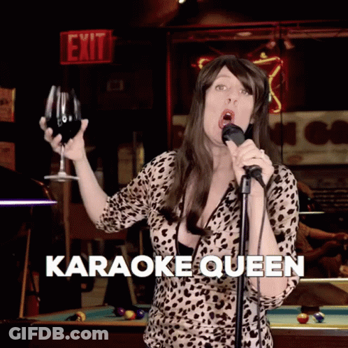 A Woman Is Singing Into A Microphone While Holding A Glass Of Wine And The Words Karaoke Queen Are Below Her GIF