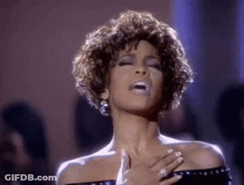 A Woman Is Singing Into A Microphone While Holding Her Hands To Her Chest . GIF