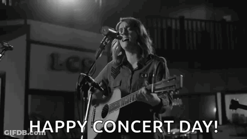 A Woman Is Singing Into A Microphone While Playing A Guitar On A Stage . GIF