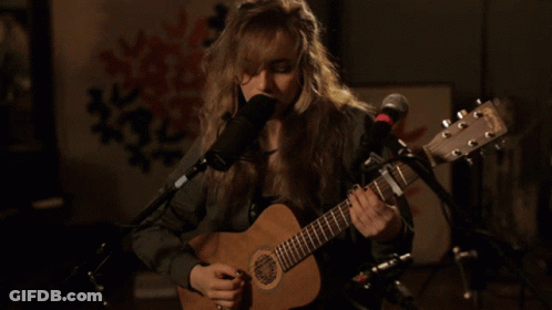A Woman Is Singing Into A Microphone While Playing A Guitar GIF