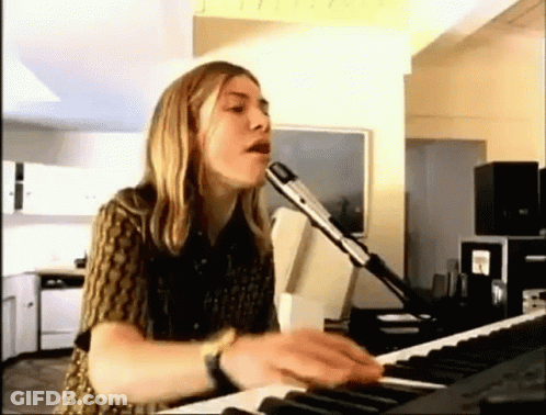 A Woman Is Singing Into A Microphone While Playing A Keyboard In A Living Room . GIF