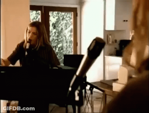 A Woman Is Singing Into A Microphone While Playing A Piano In A Room . GIF