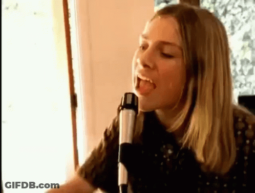 A Woman Is Singing Into A Microphone While Sitting In Front Of A Window . GIF