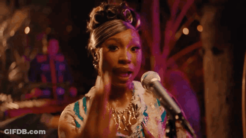 A Woman Is Singing Into A Microphone While Sitting On A Stage . GIF