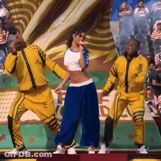 A Woman Is Singing Into A Microphone While Two Men Are Dancing In Front Of A Crowd GIF