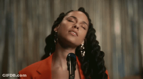 A Woman Is Singing Into A Microphone While Wearing A Red Jacket GIF
