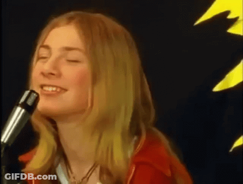 A Woman Is Singing Into A Microphone While Wearing A Red Jacket . GIF