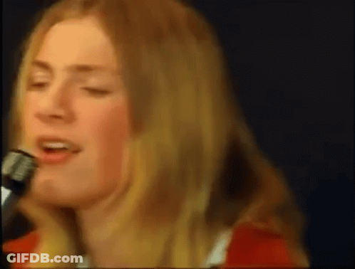 A Woman Is Singing Into A Microphone While Wearing A Red Shirt . GIF