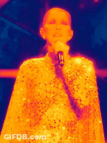 A Woman Is Singing Into A Microphone While Wearing A Sequined Cape GIF