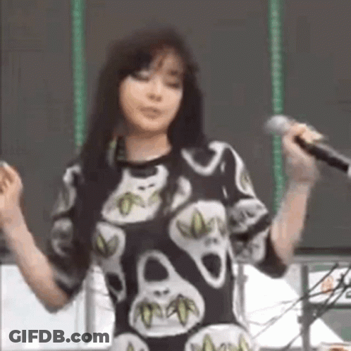 A Woman Is Singing Into A Microphone While Wearing A Skull Print Shirt . GIF