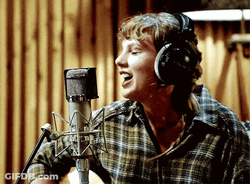 A Woman Is Singing Into A Microphone With Headphones On GIF
