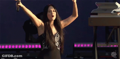 A Woman Is Singing Into A Microphone With Her Arms Outstretched GIF