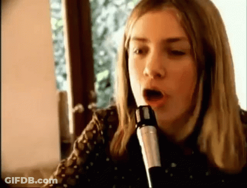 A Woman Is Singing Into A Microphone With Her Mouth Open . GIF