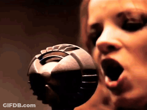 A Woman Is Singing Into A Microphone With Her Mouth Wide Open GIF