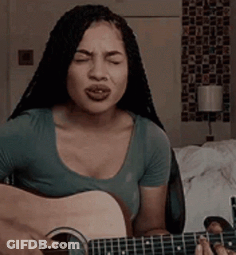 A Woman Is Singing While Playing A Guitar In A Room . GIF