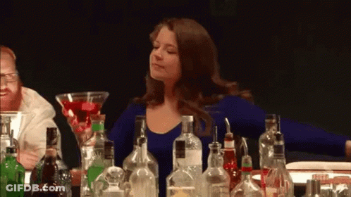 A Woman Is Sitting At A Bar Surrounded By Bottles Of Liquor . GIF