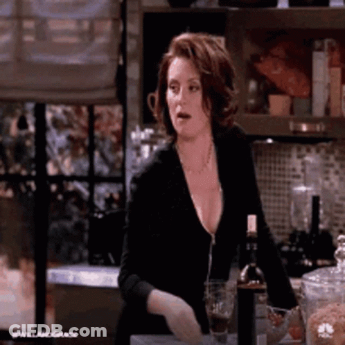A Woman Is Sitting At A Counter In A Kitchen With A Bottle Of Wine And A Glass Of Wine . GIF