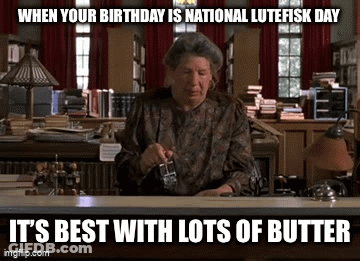 A Woman Is Sitting At A Desk In A Library Holding A Glass Of Butter GIF
