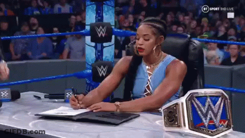 A Woman Is Sitting At A Desk In A Wrestling Ring Signing A Contract . GIF